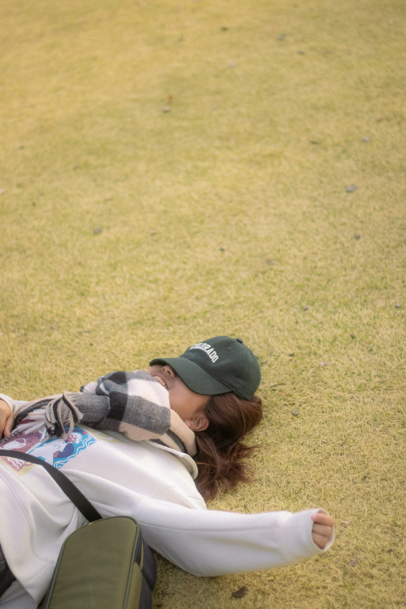 A person reclines on dry grass with an arm stretched out.