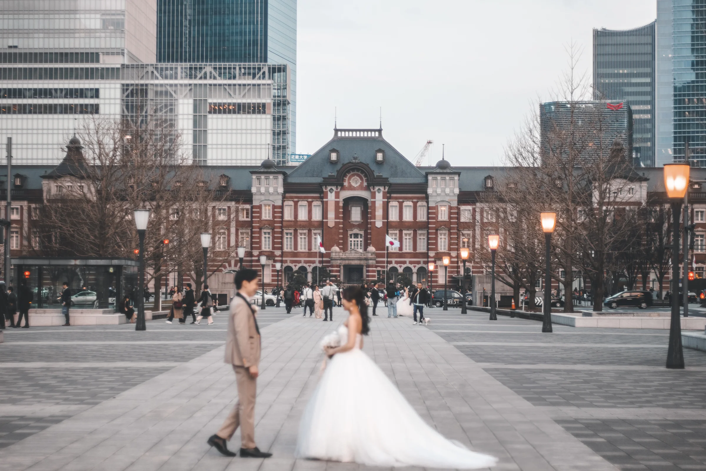 Two people in formal attire pose in the plaza before Tokyo Station.