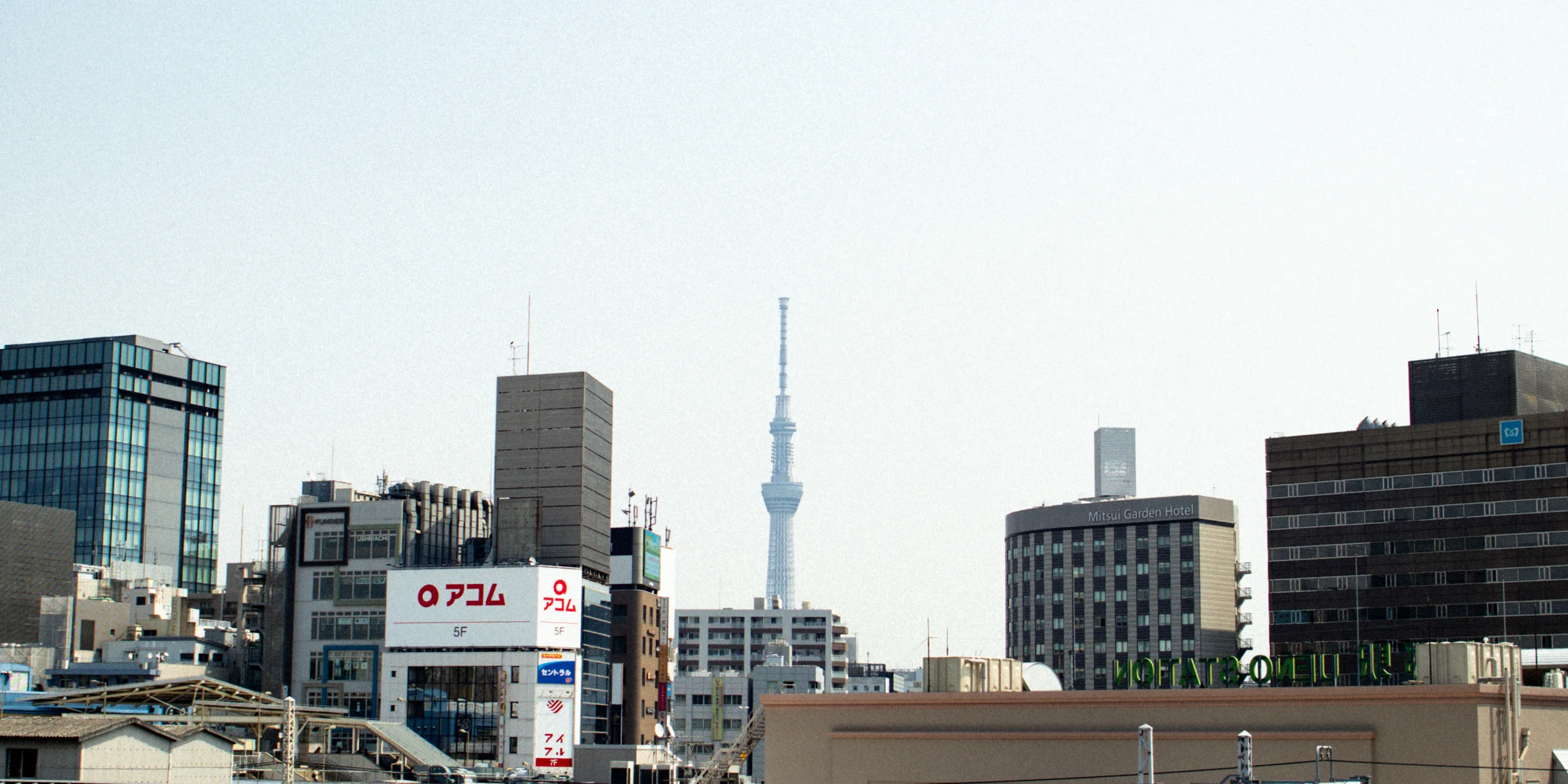 Tokyo Skytree rises above rooftops and railway lines under a pale blue sky.