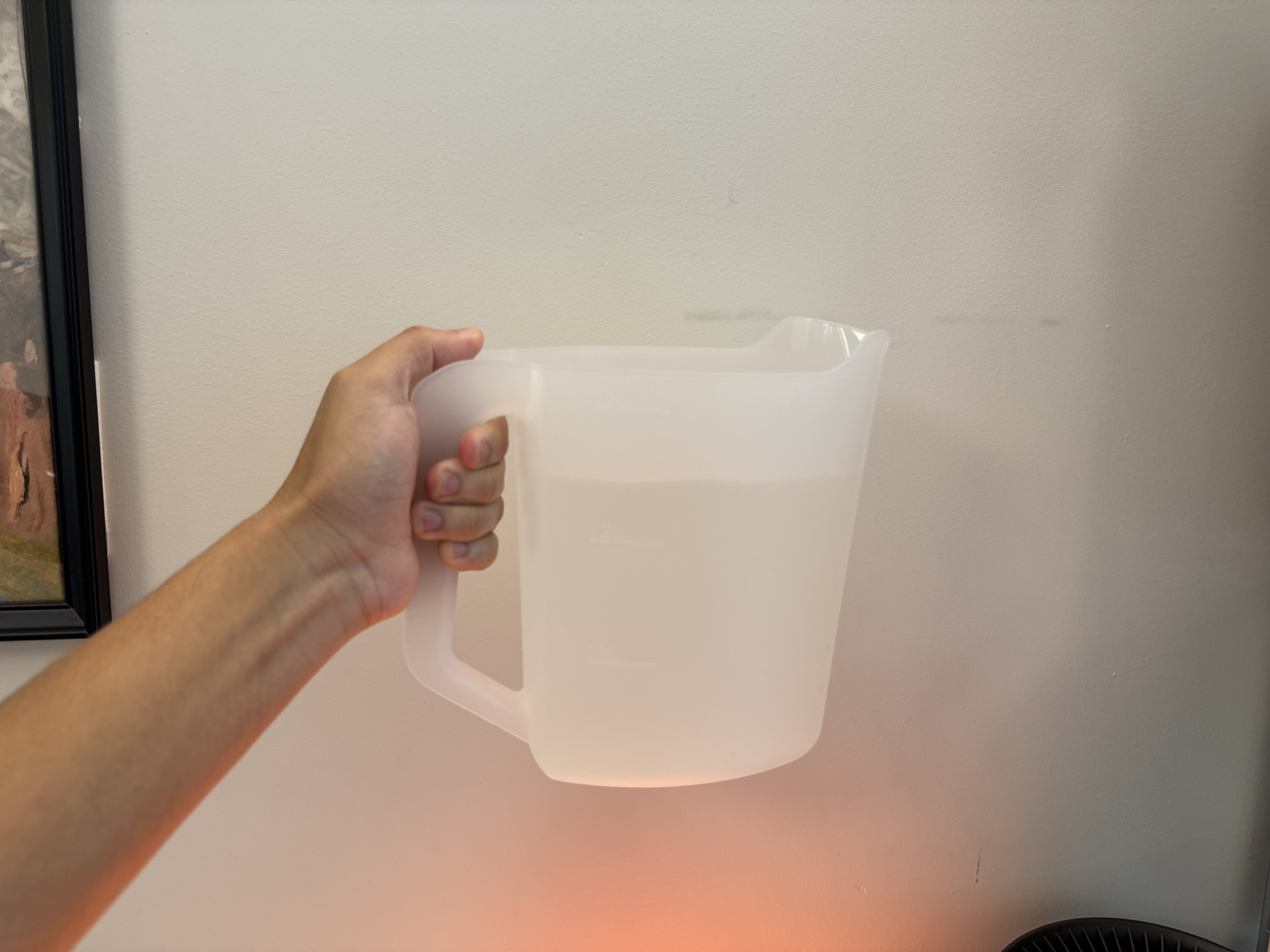 A hand holding a translucent pitcher partially filled with water.